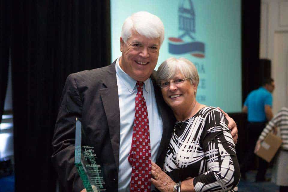 Smiling man and woman at Romano Law Group event, holding an award, in professional attire.