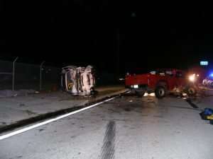 Nighttime car accident scene with overturned vehicle and damaged pickup truck.