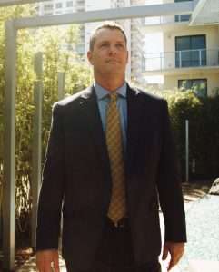 Professional man in suit outdoors near modern buildings and greenery.