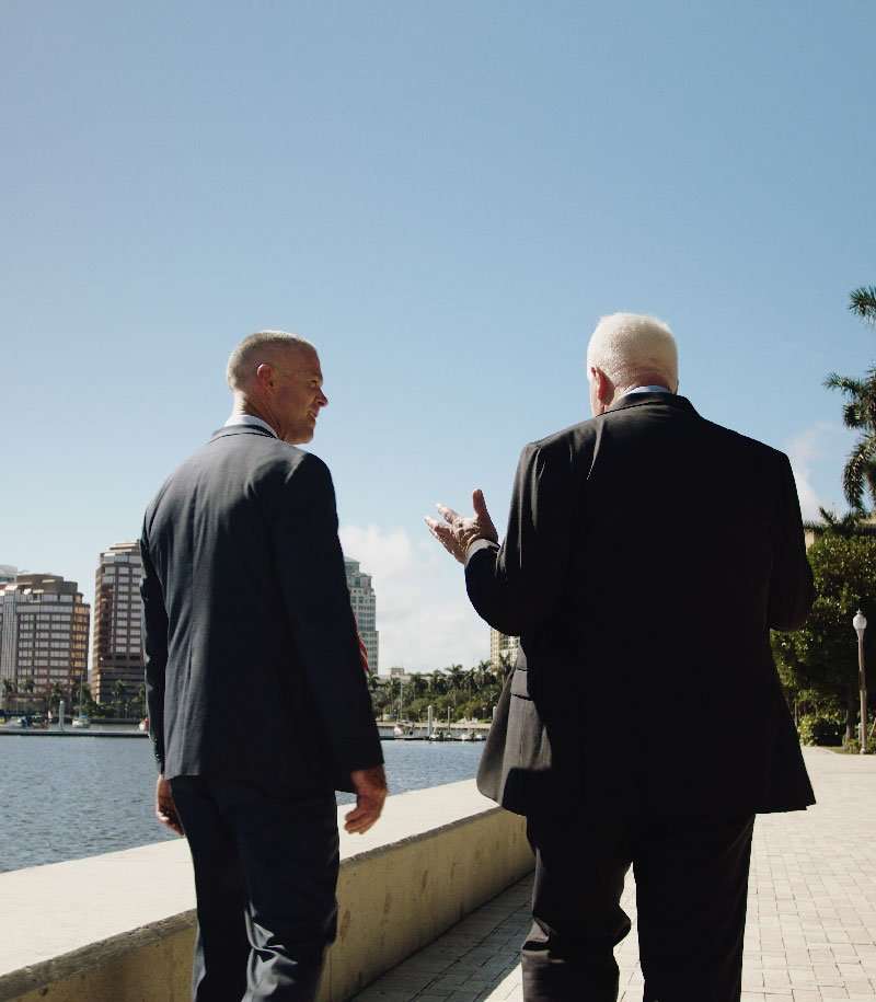 Attorneys Todd Romano and John Romano having a conversation by the waterfront in a city park.