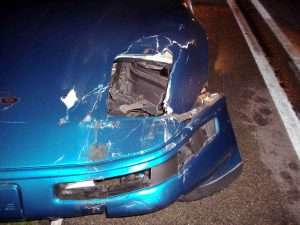 Damaged blue car with front-end crash on the road at night.