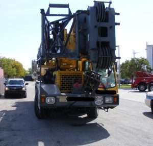 Construction crane truck parked outdoors with other vehicles in background.