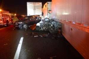 Car crash involving a semi-truck and a smaller vehicle at night, emergency responders on scene.