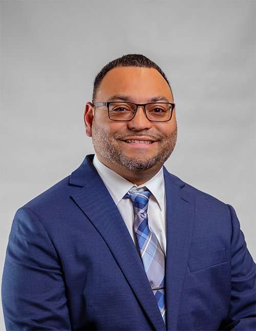 Professional portrait of a lawyer in a blue suit and glasses at Romano Law Group.