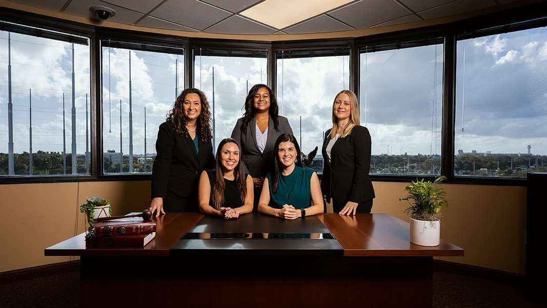Romano Law Group team of five women in a modern office with city view.