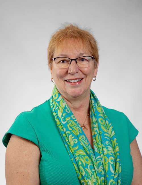 Professional woman in teal dress with colorful scarf smiling for law firm photo.