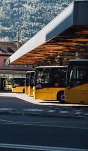 Yellow and black buses parked at a bus station with mountain backdrop.