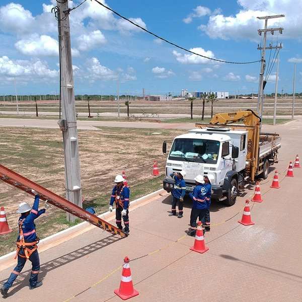 Construction workers installing utility pole on roadside with traffic cones and equipment.