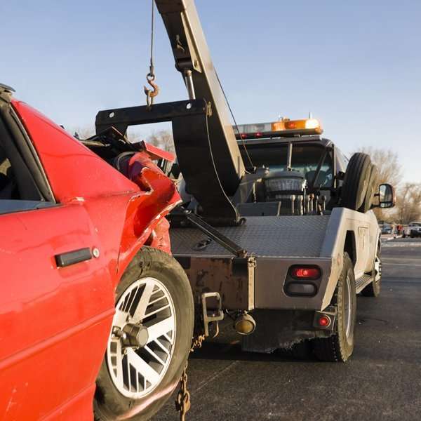 Tow truck removing damaged red car after accident on highway.