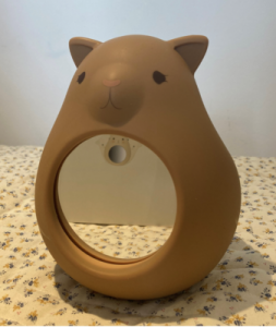 Cute bear-shaped mirror with a circular reflective surface on a floral tablecloth.