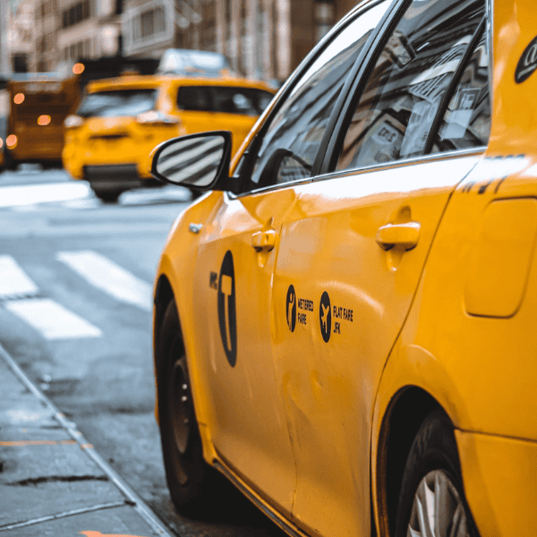 Yellow taxi cab on city street with blurred background of other taxis and buildings.