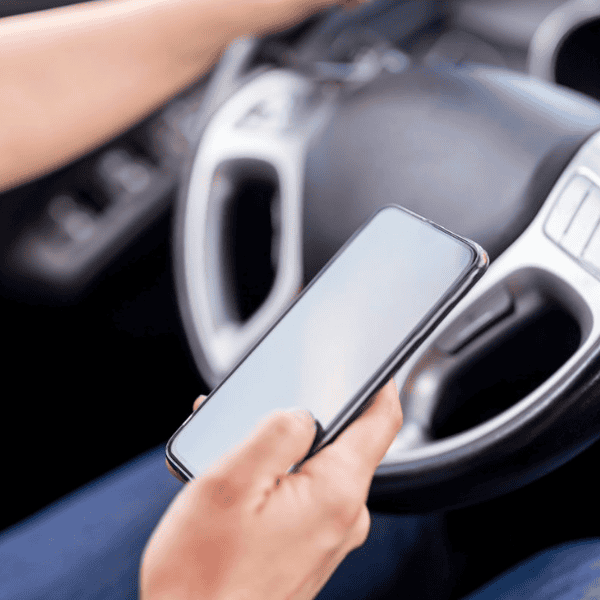 Person using smartphone while driving a car with steering wheel visible.