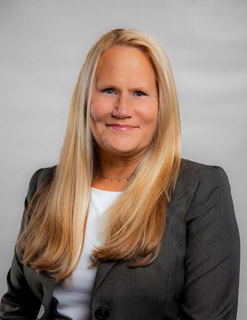 Professional woman in gray blazer smiling for a corporate portrait.
