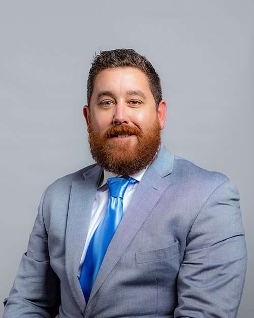 Professional lawyer in light gray suit with blue tie smiling at camera.