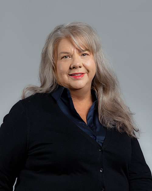 Professional woman with gray hair smiling in a dark blazer and blue shirt.
