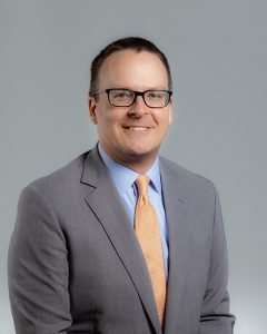 Professional lawyer in gray suit and glasses smiling for Romano Law Group.