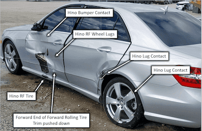 Damaged silver sedan with Hino bumper, wheel lugs, and tire, showing impact damage.