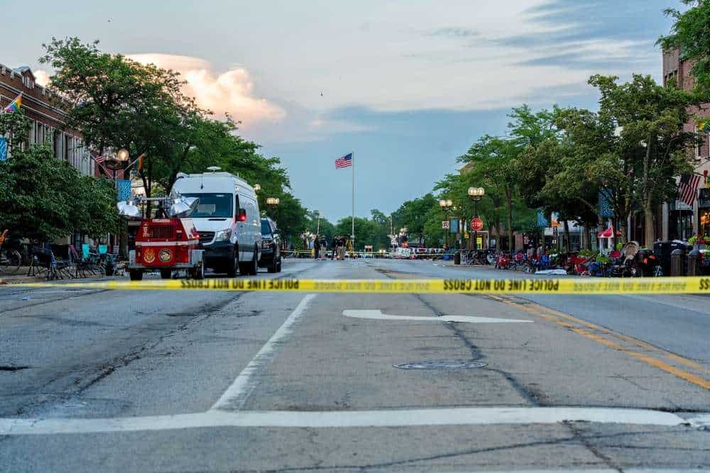 Street scene with police tape, vehicles, and trees in a small town.