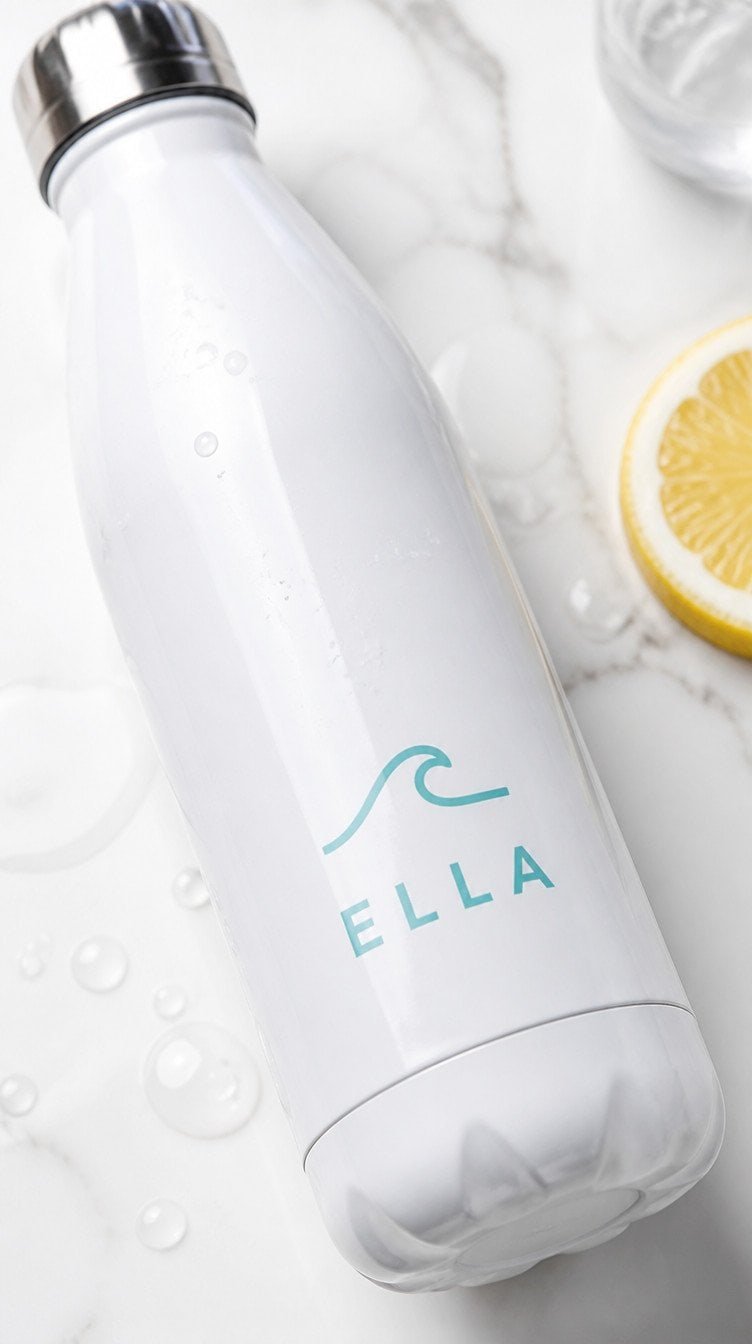 White stainless steel water bottle with teal wave icon and ELLA iron-on vinyl on white marble surface with lemon