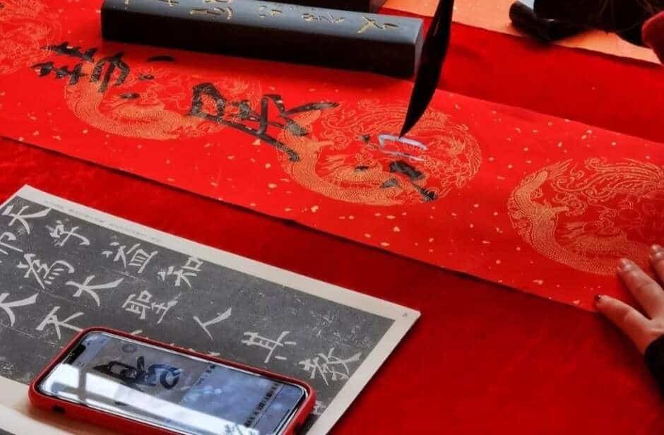 Traditional Lunar New Year craft of writing spring couplets with a brush on red paper, featuring intricate dragon patterns and ink tools