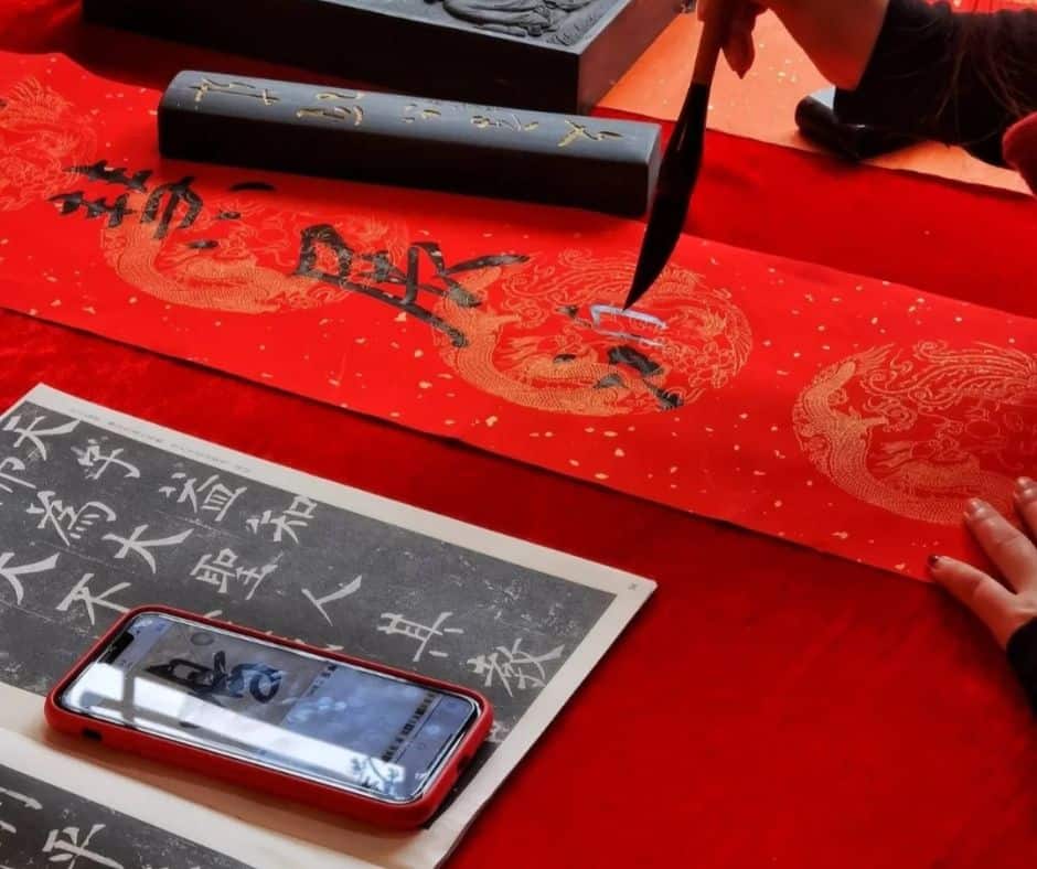 Traditional Lunar New Year craft of writing spring couplets with a brush on red paper, featuring intricate dragon patterns and ink tools
