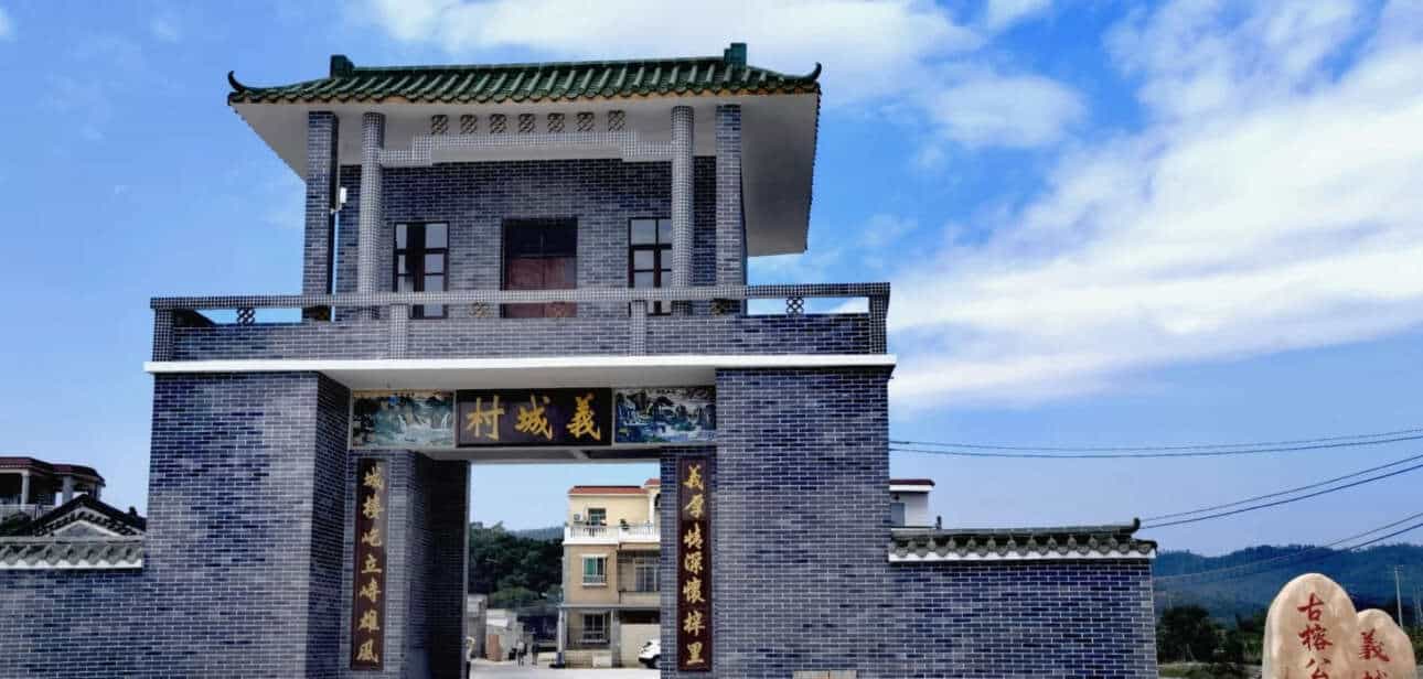 Entrance gate of Yicheng Ancient Banyan Park in Taishan Duhu, featuring traditional architecture with a tiled roof and stone sign under a clear blue sky.