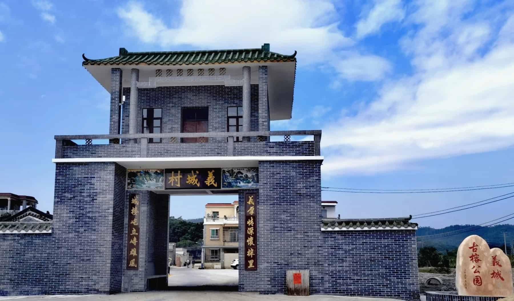 Entrance gate of Yicheng Ancient Banyan Park in Taishan Duhu, featuring traditional architecture with a tiled roof and stone sign under a clear blue sky.