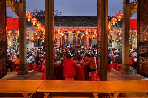 Traditional Chinese New Year celebration with an elderly man in red attire standing under red lanterns and Spring Festival couplets.