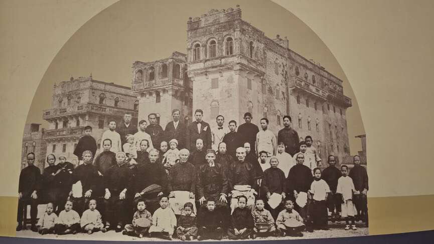 Historical photograph of a large Taishanese family in front of iconic diaolou towers, showcased at Taishan Overseas Chinese Culture Museum.