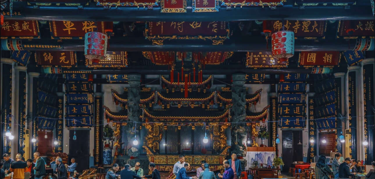People gathered inside a Chinese ancestral hall with ornate decorations, banners, and altars, preserving Chinese genealogy traditions during a communal event.