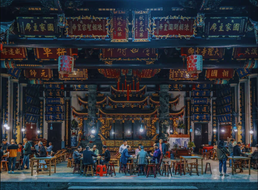 People gathered inside a Chinese ancestral hall with ornate decorations, banners, and altars, preserving Chinese genealogy traditions during a communal event.