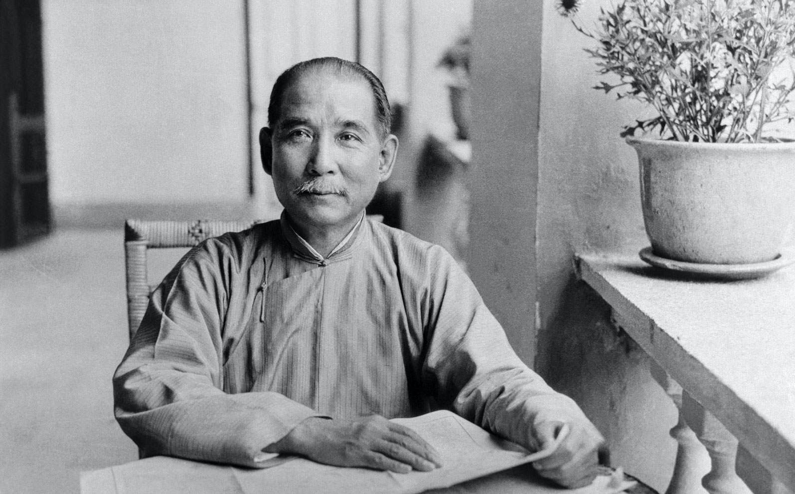Historical photo of Sun Yat-Sen seated at a table reading in Guangzhou, showcasing his dedication to learning and revolutionary ideals.