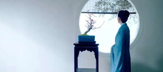 Woman in blue robe gazing at a plum blossom bonsai through a round window, embodying inward reflection in Tianxia aesthetics