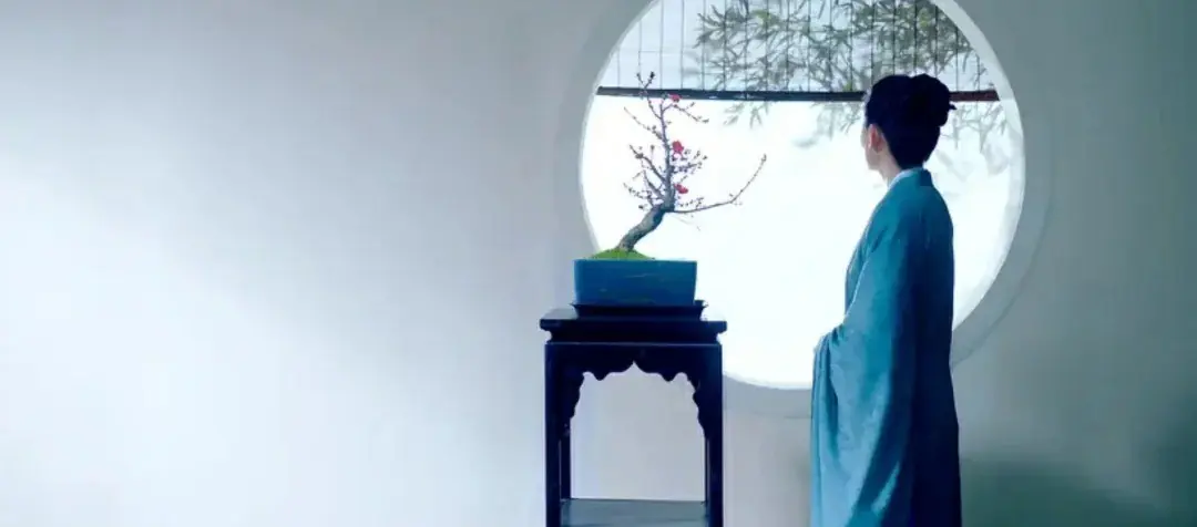 Woman in blue robe gazing at a plum blossom bonsai through a round window, embodying inward reflection in Tianxia aesthetics