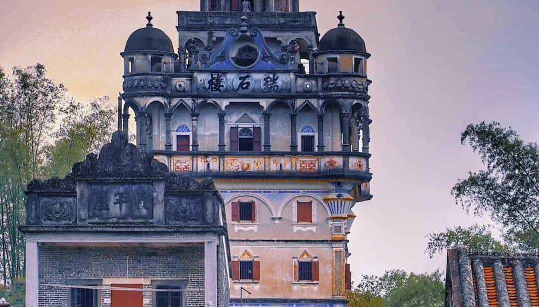Diaolou watchtowers rising from rice paddies at Zili Village in Kaiping, with a first-time roots trip visitor standing at the village entrance