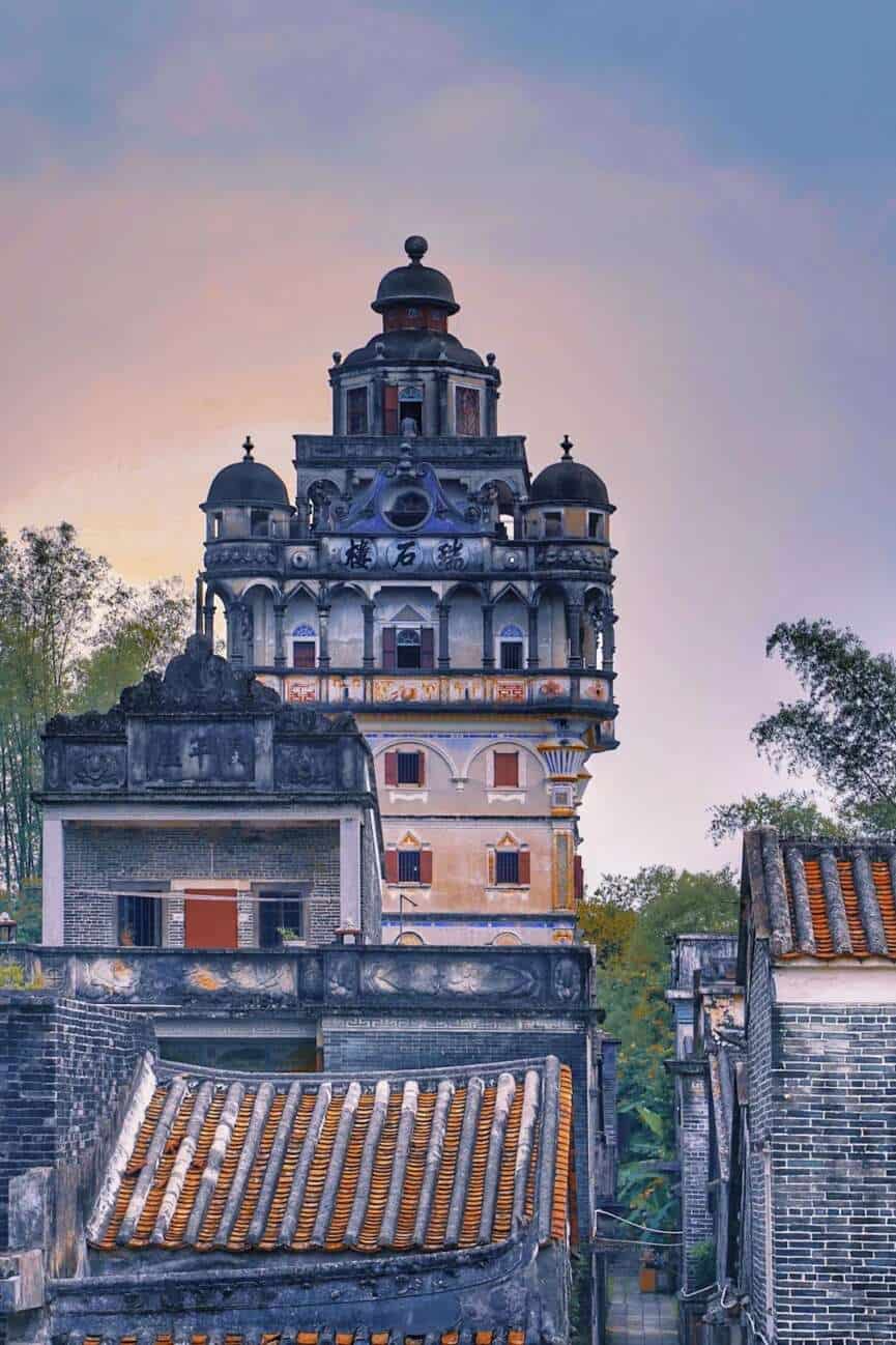 Diaolou watchtowers rising from rice paddies at Zili Village in Kaiping, with a first-time roots trip visitor standing at the village entrance
