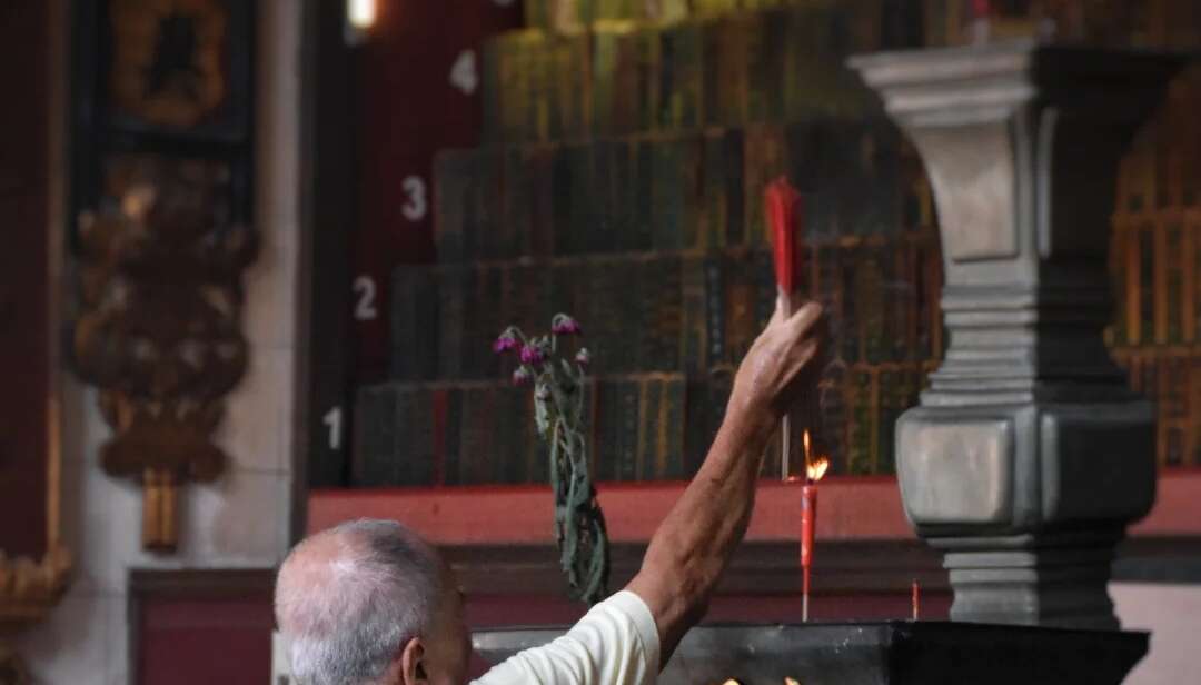 Elder placing incense at an ancestral altar inside a traditional Chinese clan temple during the Qingming Festival.