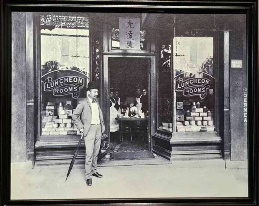 A vintage photograph of a Chinese restaurant storefront in a North American Chinatown, its proprietor posed outside — the overseas businesses that anchored diaspora community life.