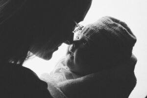 Schwarz-weiß-Fotografie im Gegenlicht von einer Mutter und ihrem Baby im Fotostudio Rostock, die sich mit den Nasen sanft berühren und innigen Blickkontakt teilen.