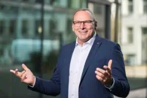 Bewerbungsfotos im Rostocker Fotostudio – Dynamisches Business-Porträt eines lächelnden Mannes in blauem Anzug mit offener Gestik vor einem modernen Hintergrund.