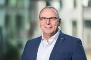 Bewerbungsfotos im Rostocker Fotostudio – Professionelles Business-Porträt eines Mannes mit Brille im blauen Anzug vor einem modernen, unscharfen Hintergrund.