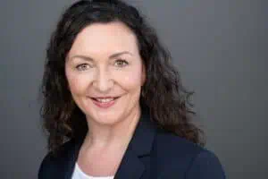 Bewerbungsfotos im Rostocker Fotostudio – Professionelles Business-Portrait einer Frau mit lockigen dunklen Haaren, freundlichem Lächeln und dunklem Blazer vor grauem Hintergrund.