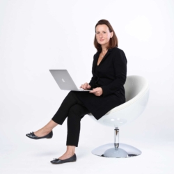 Bewerbungsfotos im Rostocker Fotostudio – Business-Porträt einer Frau in schwarzem Outfit mit Laptop auf einem modernen weißen Stuhl vor hellem Hintergrund.