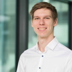 Professionelles Business-Portrait eines Mitarbeiters des Frauenhofer Instituts vor Ort, welches einem modernen Bewerbungsfoto ähnelt. Der Mann hat kurzes braunes Haar, mit freundlichem Lächeln und weißem Hemd vor modernem, verglastem Hintergrund.
