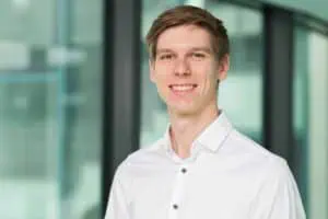 Professionelles Business-Portrait eines Mitarbeiters des Frauenhofer Instituts vor Ort, welches einem modernen Bewerbungsfoto ähnelt. Der Mann hat kurzes braunes Haar, mit freundlichem Lächeln und weißem Hemd vor modernem, verglastem Hintergrund.