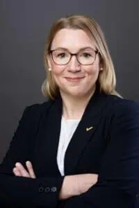 Bewerbungsfotos im Rostocker Fotostudio – Professionelles Business-Portrait einer Frau mit Brille, blonden Haaren und dunklem Blazer vor dunklem Hintergrund.