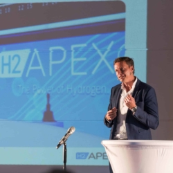 Peter Rößner von APEX hält eine Präsentation über Wasserstofftechnologie auf einer Fachkonferenz, mit einer großen Projektion des H2APEX-Logos im Hintergrund – aufgenommen vom Businessfotograf in Rostock.