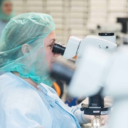Laborantin mit Haarschutz und Kittel analysiert Proben unter einem Mikroskop in einem Reinraum – aufgenommen vom Businessfotograf in Rostock.