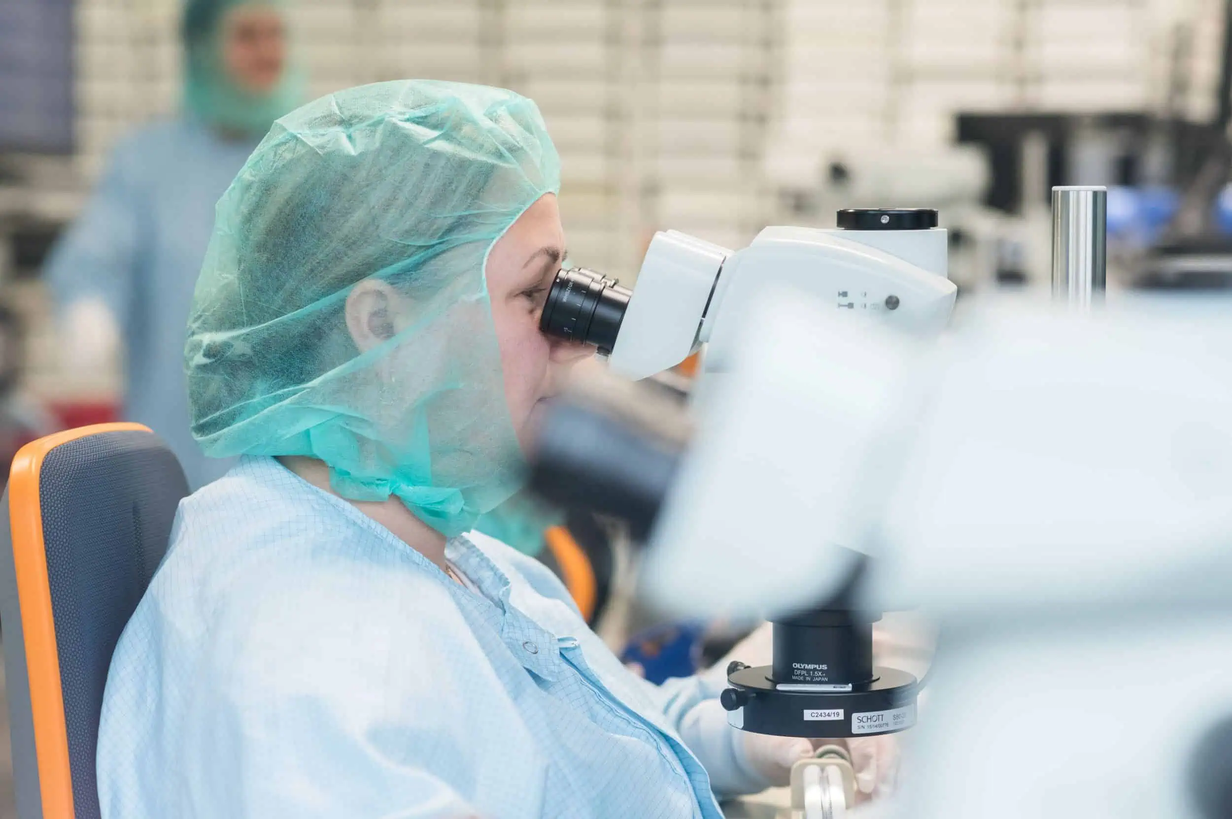 Hochpräzise Laborarbeit einer Wissenschaftlerin Laborantin mit Haarschutz und Kittel analysiert Proben unter einem Mikroskop in einem Reinraum – aufgenommen vom Businessfotograf in Rostock.
