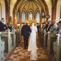 Kirchliche Hochzeit in Warnemünde mit Braut im weißen Kleid beim emotionalen Einzug in die historische Kirche mit Gästen und maritimer Atmosphäre.